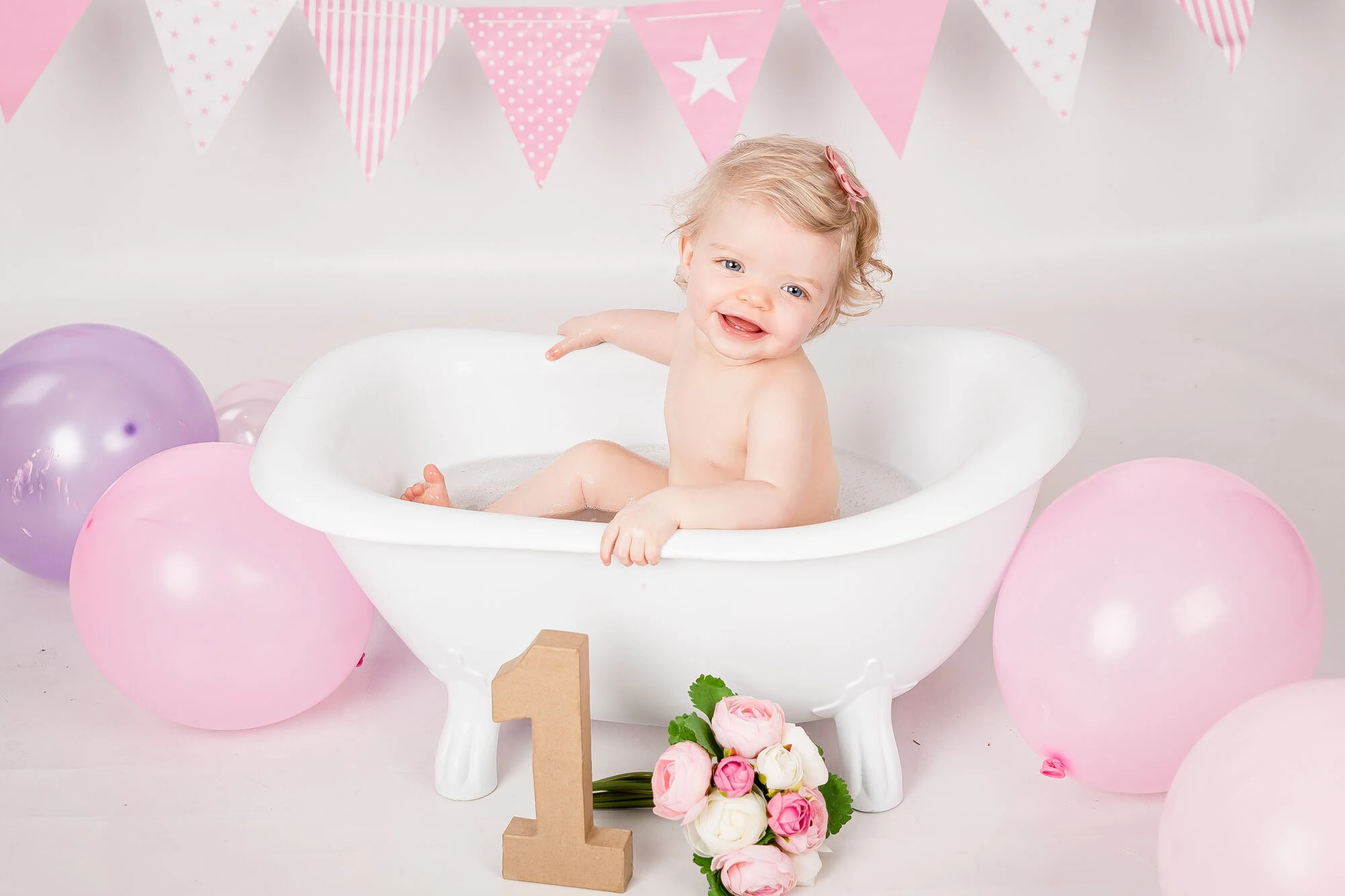 Pink and white balloon cake smash setup with a freestanding bath tub and florals