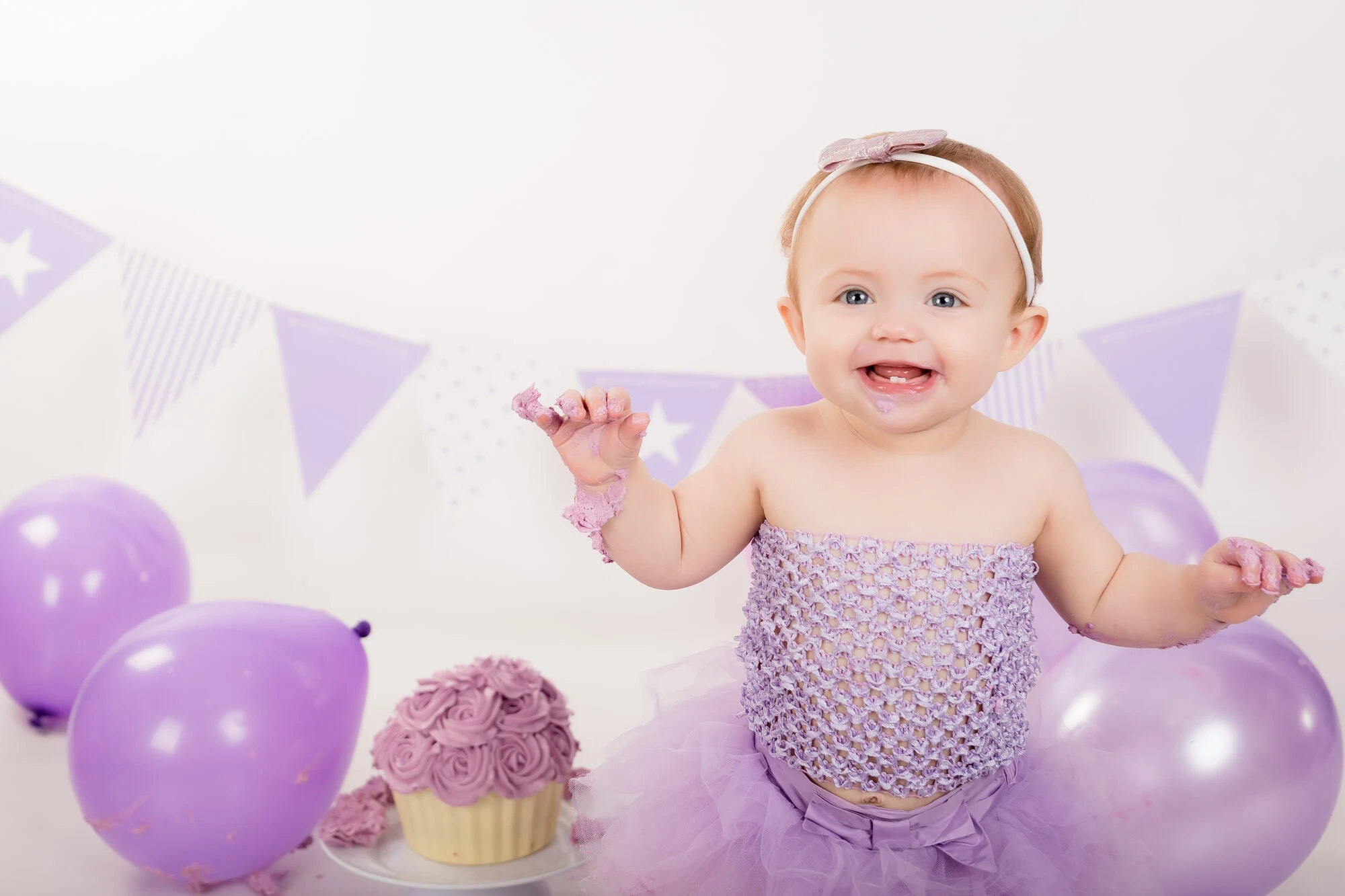 Purple bunting and balloon cake smash setup with a cupcake stand
