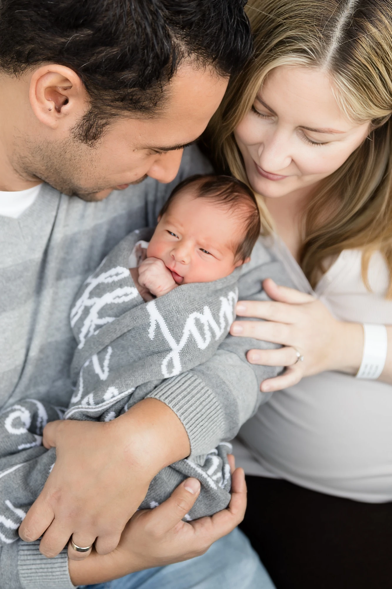 Parents holding their newborn at the hospital bedside, mum still wearing her hospital wristband